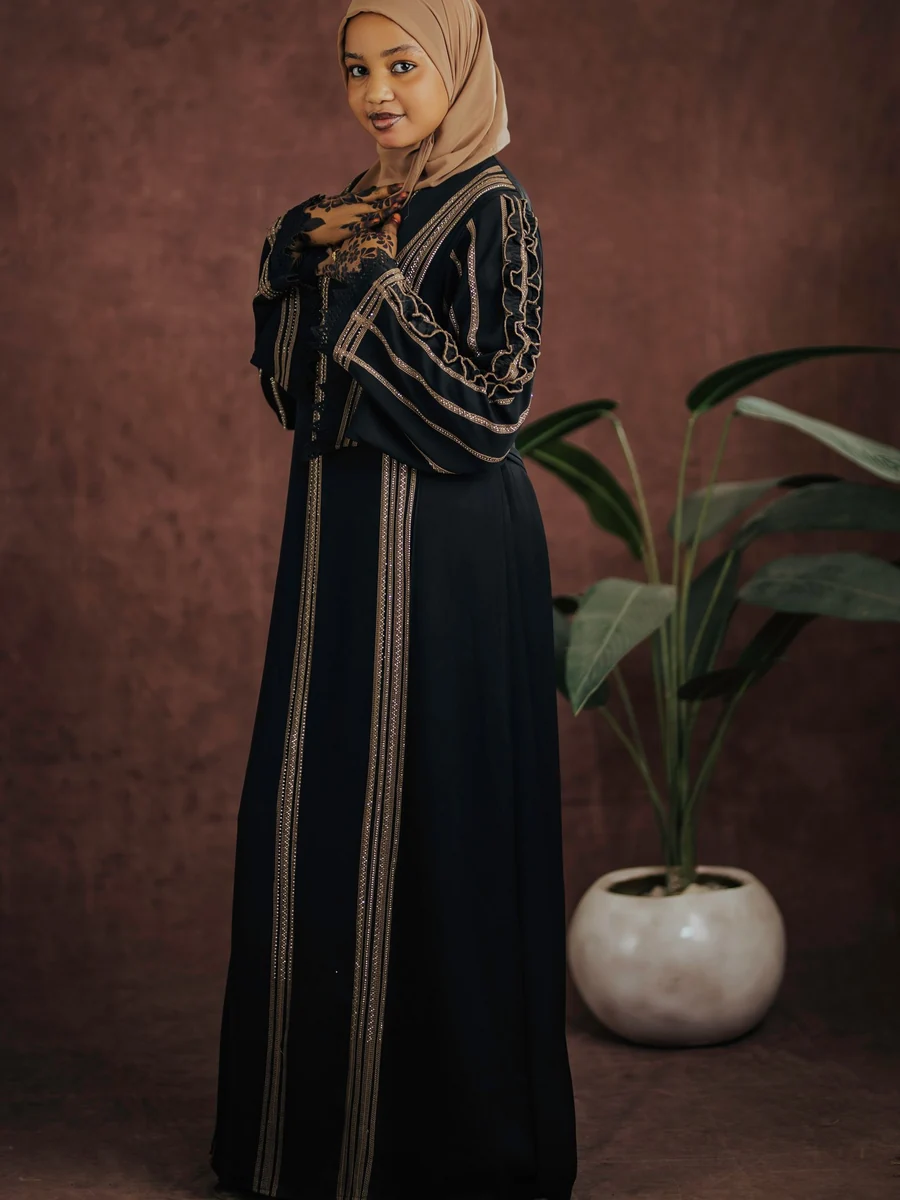 Illustrative: closed abaya wholesale — a full-length black abaya, closed at the front, with gold trim. Licensed stock photograph, not our own product.
