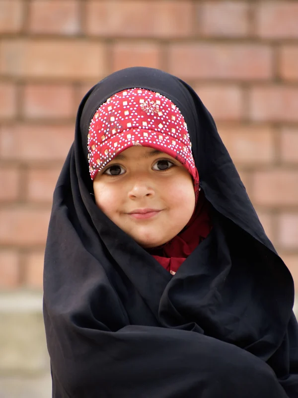 Illustrative: a young girl in a long black abaya and patterned cap. Licensed stock photograph, not our own product.