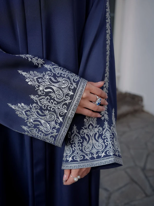 Illustrative: white embroidery on the sleeve of a navy abaya, close up. Licensed stock photograph, not our own product.