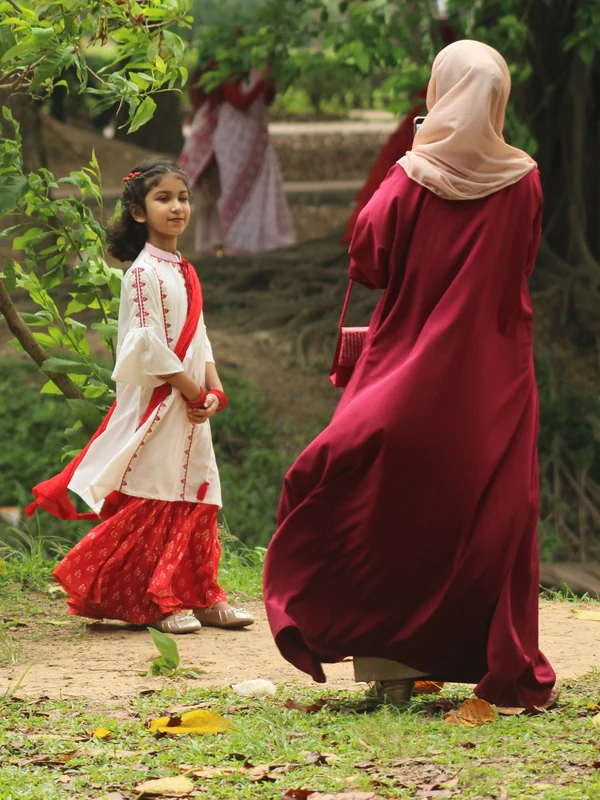Illustrative: a girl and a woman in long traditional dresses walking in a park. Licensed stock photograph, not our own product.
