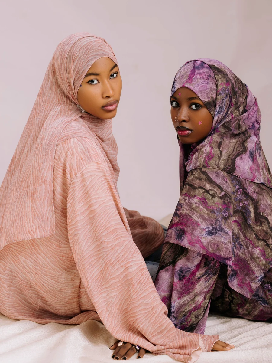 Illustrative: wholesale hijab supplier — two women in pink and purple hijabs matched to their outfits. Licensed stock photograph, not our own product.