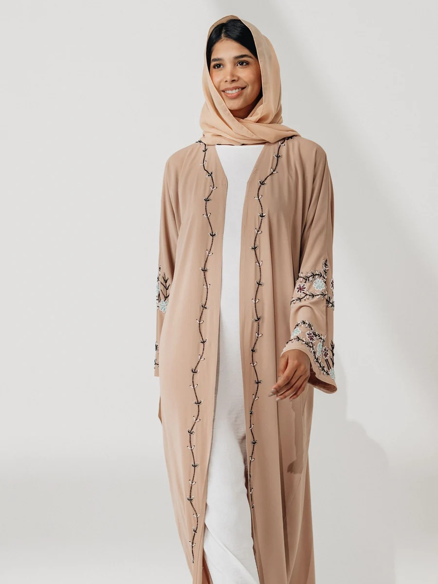Wholesale open abaya: a beige open abaya with embroidered edges over a white inner dress (illustrative stock photo)