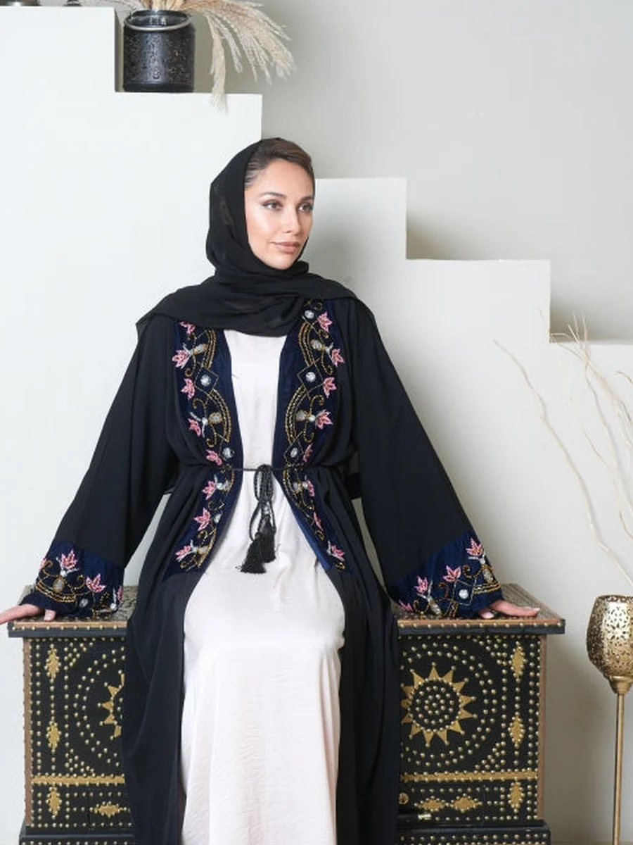 A black open abaya with floral embroidery worn over a white dress (illustrative stock photo)