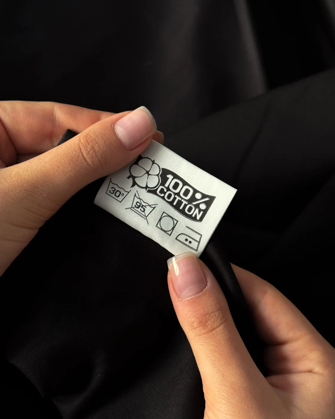Private label abaya manufacturer: checking a sewn-in care label on black fabric (illustrative stock photo)