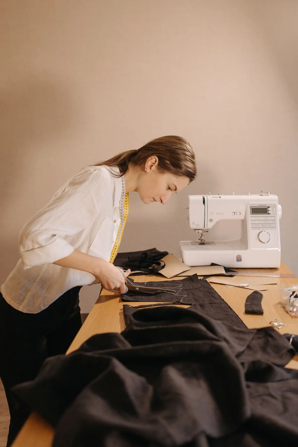 Illustrative stock photo: a tailor cutting black fabric by hand on a cutting table