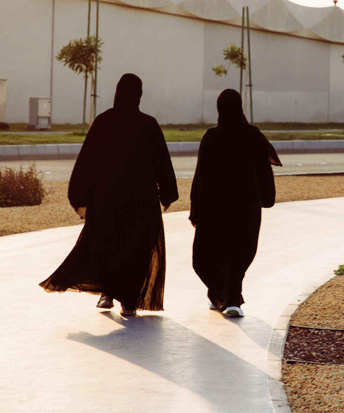 Two women in flowing black abayas walking along a path in evening light, wholesale abayas from Dubai
