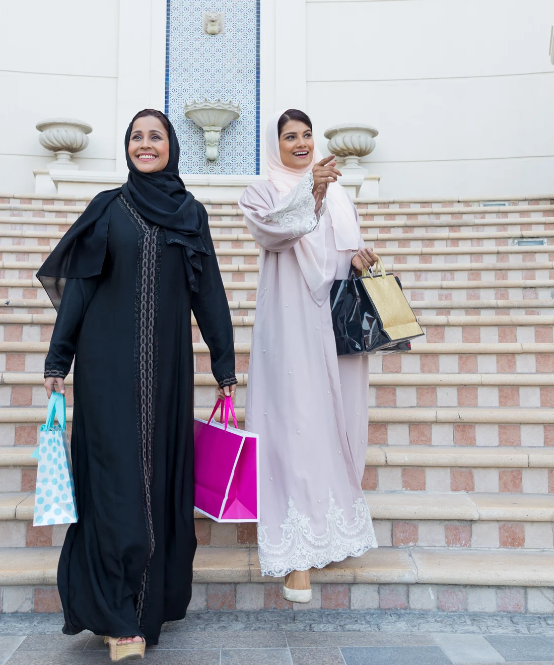 Black and blush abayas worn with shopping bags on a marble staircase, abaya wholesale supplier in Dubai